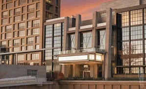 Modern buildings with large windows reflecting the sunset, and a lit marquee entrance.