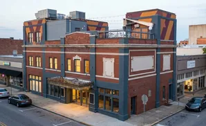 A historic brick building with blue accents and a colorful patterned upper story on a city street.