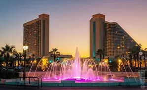 A lit fountain in front of two modern hotels at sunset.