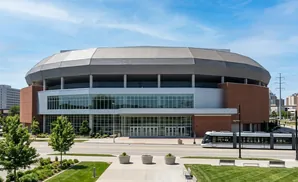 Modern stadium with a large glass facade and a streetcar passing by.