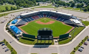 Aerial view of a baseball stadium with a green field, blue and red seats, and a large scoreboard.