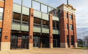 Red brick building with multiple levels, windows, and railings. A metal fence is in the foreground.