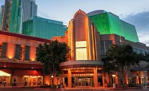 Art Deco entrance to a casino with green glass buildings in the background at dusk.