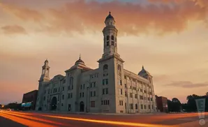 Large, ornate building with two towers at sunset, light trails on the road in foreground.