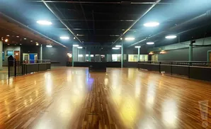 A wide, empty dance floor with a polished wooden floor, dark walls, and track lighting.