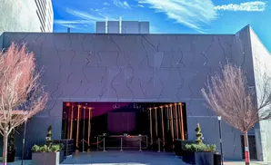 Modern dark building with a grand entrance featuring illuminated pillars and red velvet ropes.