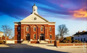 A brick building with a white dome and tower stands against a dramatic sunset sky with blue and purple clouds.