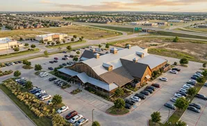Aerial view of a large barn-style building with a parking lot full of cars.