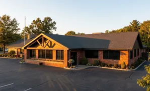 Exterior view of a single-story brick building with large windows, a gabled roof, and landscaping, bathed in warm evening light.