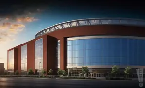 A modern stadium with a curved, glass facade and red brick accents under a dramatic sunset sky.