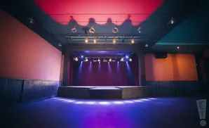 An empty music venue stage with purple lighting and red curtains.