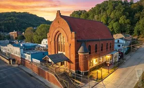 Aerial view of an old brick church with a red roof in a town at sunset.
