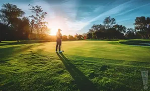 Golfer on a green fairway at sunset, long shadow cast by the setting sun.