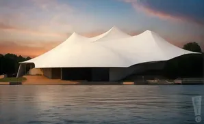 A white, tent-like amphitheater stands beside a body of water at sunset.