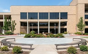 Modern brick building with large windows, curved benches, and manicured landscaping under a clear blue sky.