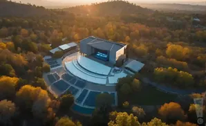 An aerial view of an outdoor amphitheater surrounded by autumn trees, bathed in golden hour light.