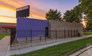 A purple and brick building with a large billboard against a colorful sunset sky.