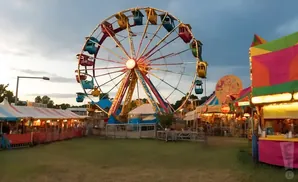 A Ferris wheel at a carnival with colorful tents and booths.