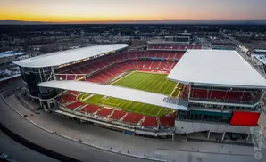 Aerial view of a football stadium with red seats and a green field at sunset.