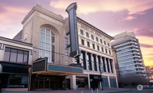 A historic theater with a marquee and a modern high-rise building at sunset.