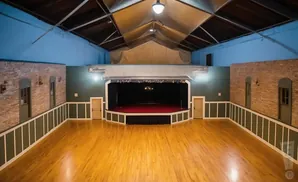 An empty ballroom with a stage, wooden floors, and exposed beams on the ceiling.