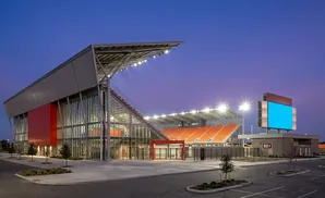 Modern soccer stadium with orange seats and a large blue scoreboard at dusk.
