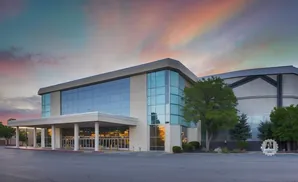A modern building with large glass windows and a covered entrance under a colorful sunset sky.
