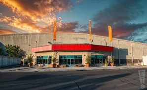 Exterior of a building with a red awning and large windows, under a dramatic sunset sky.