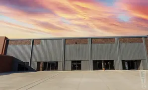 A modern industrial building with corrugated metal siding and a colorful sunset sky.