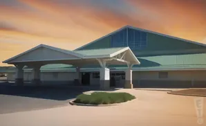 A building with a green roof and white covered entrance, set against a sunset sky.