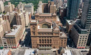 Aerial view of Carnegie Hall and surrounding Manhattan buildings, with trees and Central Park in the background.