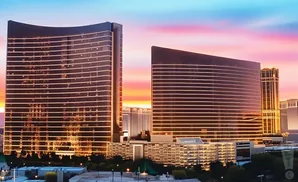 Two modern skyscrapers with illuminated horizontal lines reflect a colorful sunset sky.