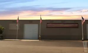 An American flag flies in front of a warehouse with a large garage door under a colorful sunset sky.