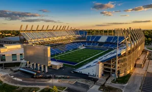 Aerial view of a modern football stadium with blue seats and a green field, at sunset.