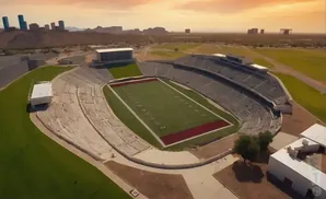 Aerial view of a football stadium with desert landscape and city skyline in the background.