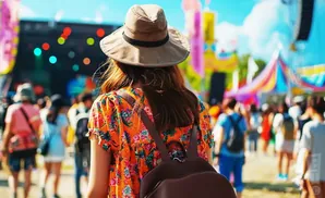 A woman in a floral dress and hat walks through a lively festival with colorful decorations and blurred crowds.