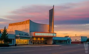 An old movie theater with a marquee and vertical sign illuminated at sunset.