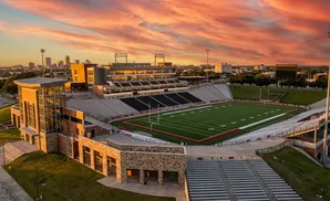 An aerial view of a football stadium at sunset, with a vibrant orange and pink sky.