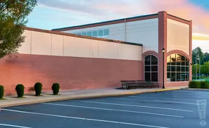 Modern building with red brick and cream siding, large arched windows, and a parking lot.