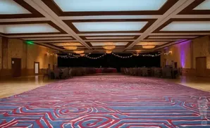 A grand ballroom with a red and blue patterned carpet, a coffered ceiling, and tables set up for an event.