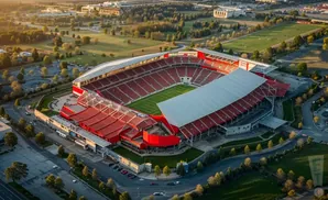 Aerial view of a large, red-seated football stadium with a white roof at sunset.