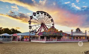 A ferris wheel and carnival rides at sunset with colorful clouds.