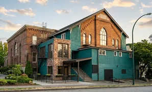 An old brick building with teal siding, featuring arched windows and an exterior staircase.