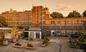 Courtyard of a brick industrial building with trees and outdoor seating.