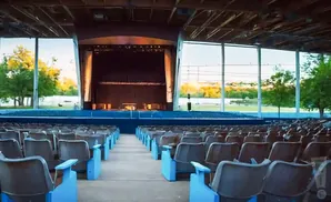An empty outdoor amphitheater with rows of brown seats and a stage in the background.