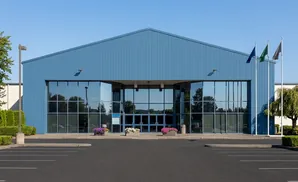 Blue building with large glass windows, parking lot, and three flags on the right.