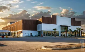 Modern warehouse with wood and white siding, large windows, and palm trees under a cloudy sky.
