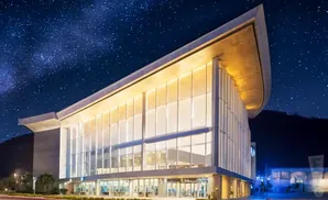 Modern building with glass facade lit up at night under a starry sky.