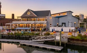 A waterfront brewery with outdoor seating and picnic tables at sunset.