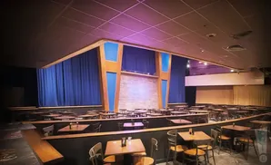Comedy club stage with blue curtains, brick wall, and many tables and chairs.